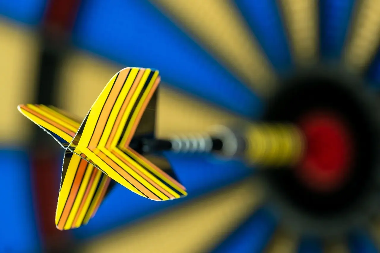 Dartpil med gule stribede fjer mod sløret dartskive